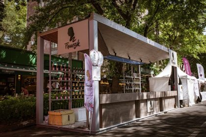 Barraca de vinhos em um evento ao ar livre, cercada por árvores e visitantes.