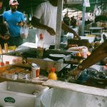 Vendedores e clientes movimentam uma feira de rua em São Paulo, com barracas de comida ao ar livre.