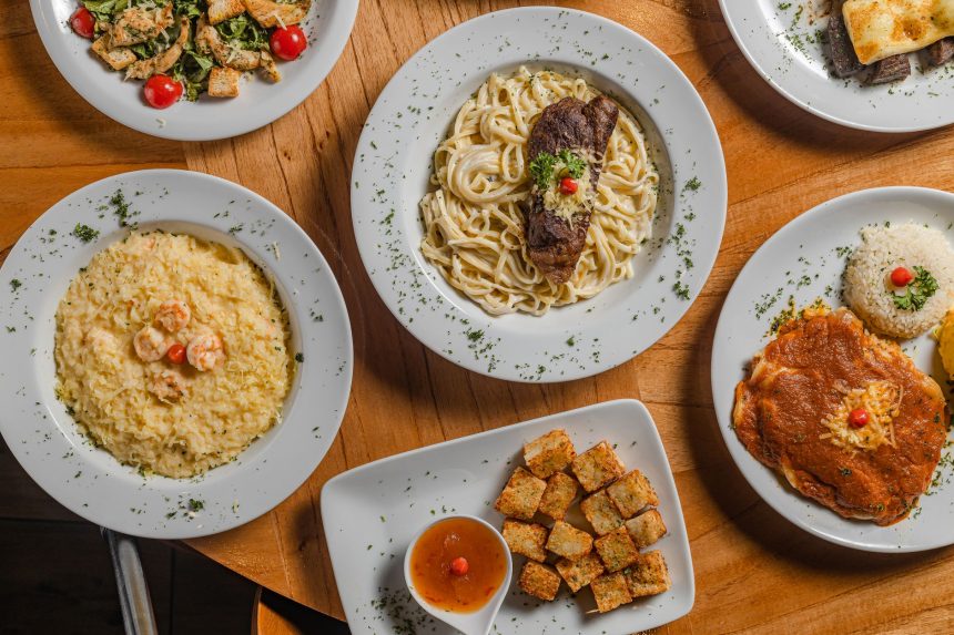 Vista de cima de diversos pratos gourmet brasileiros dispostos sobre uma mesa.