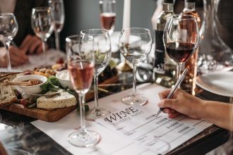 Mesa de degustação com taças de vinho, queijos e anotações de avaliação em um ambiente interno.